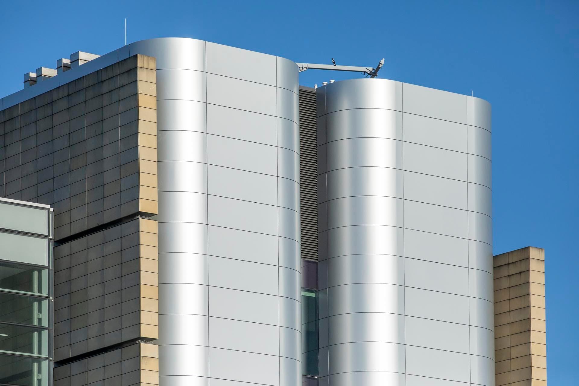 Upper façade of the Charles Perkins Centre highlighting curved Alpolic NC silver panels alongside beige vertical cladding.
