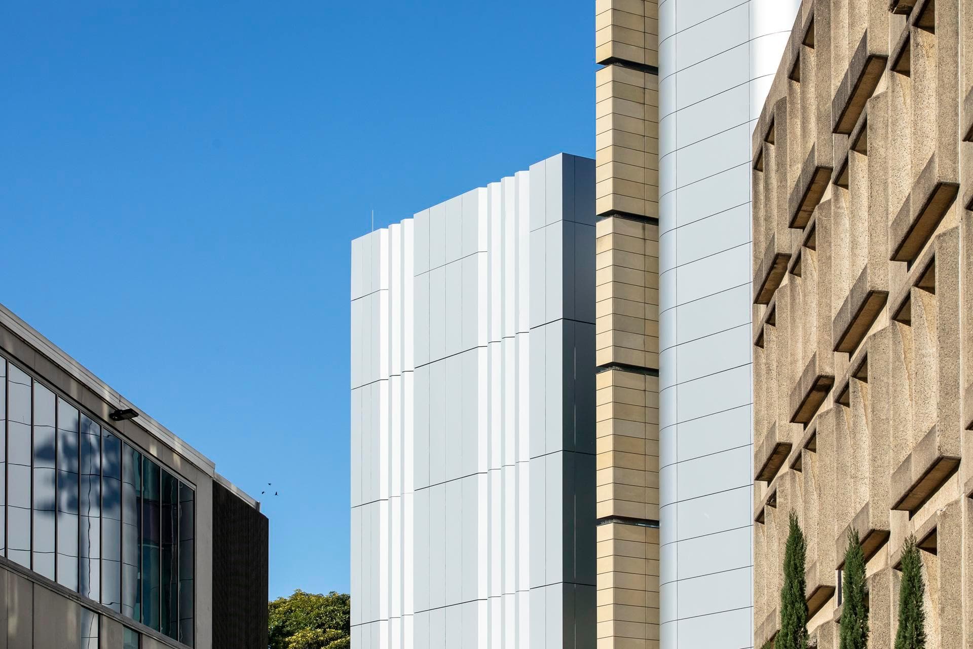 Side view of Charles Perkins Centre showing Alpolic NC silver and beige façade panels contrasted with adjacent concrete building.