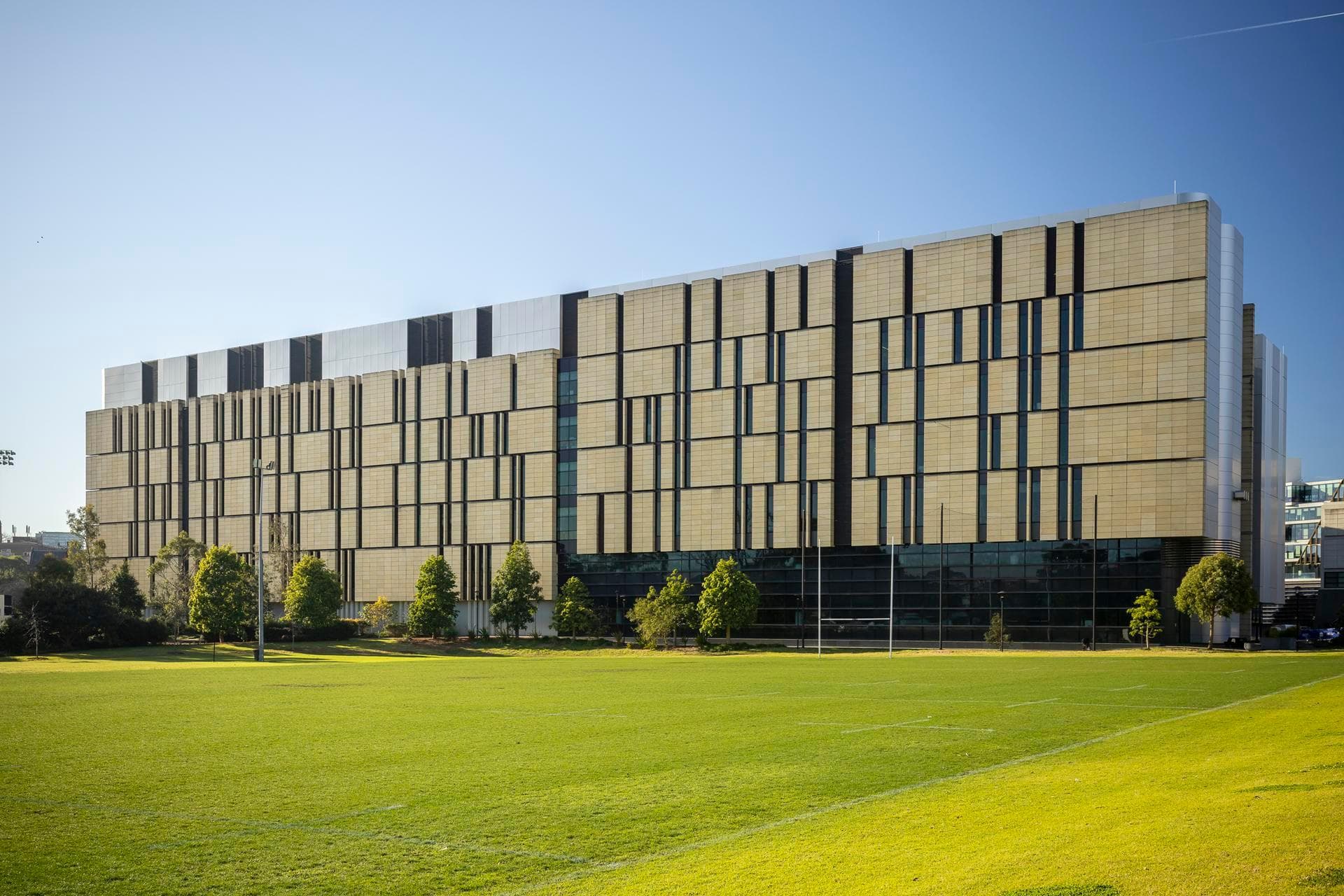 Wide elevation of the Charles Perkins Centre with Alpolic NC beige cladding panels and vertical silver accents across the façade.