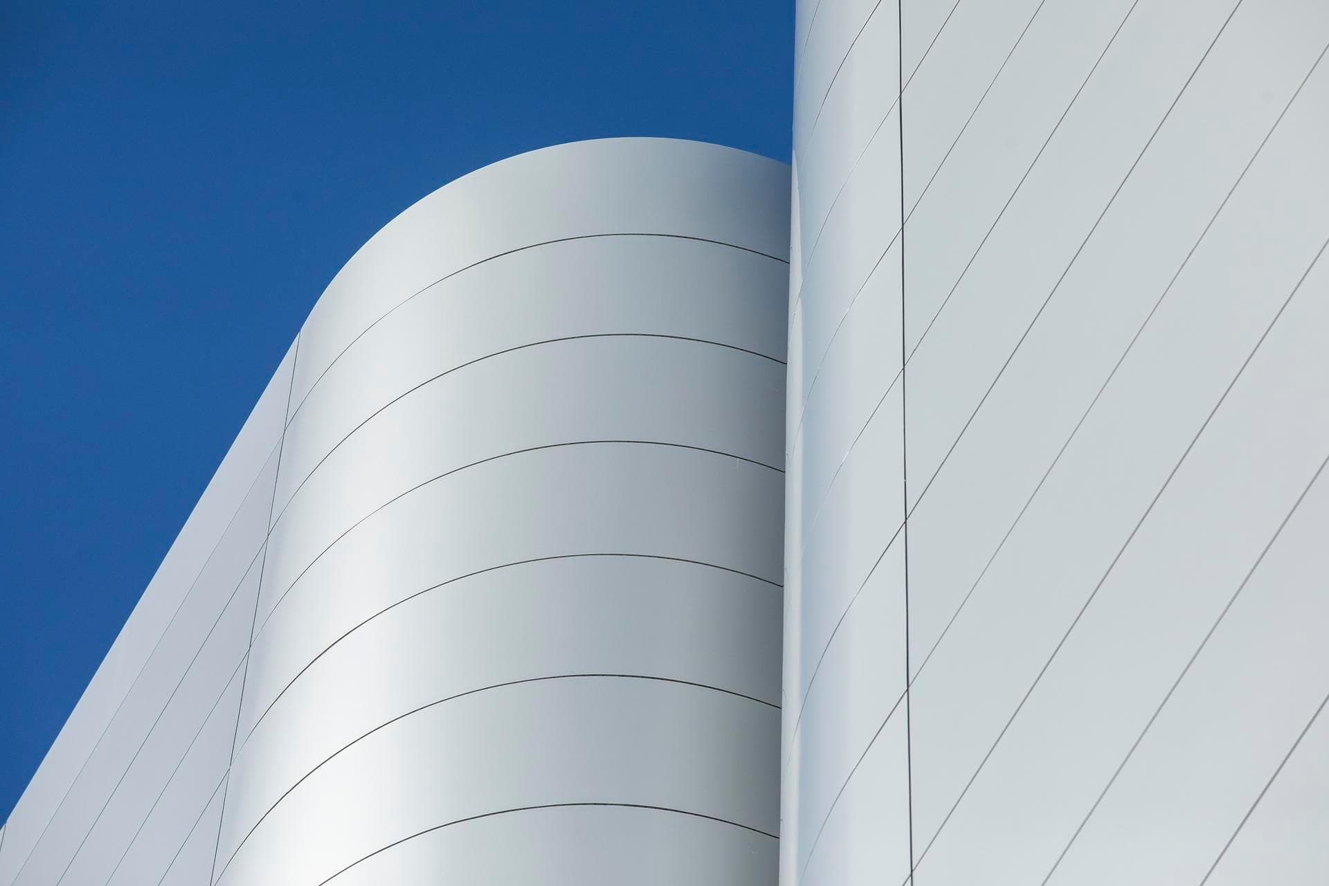 Curved Alpolic NC silver façade panels on the Charles Perkins Centre, photographed against a clear blue sky.